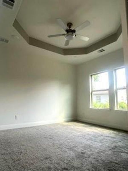 Carpeted spare room featuring a tray ceiling and ceiling fan