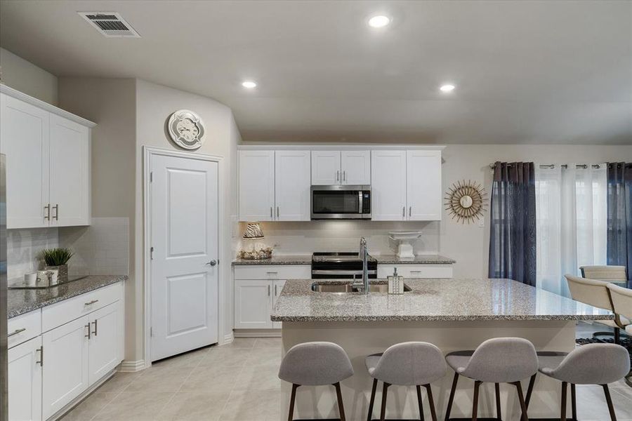 Appliances stay with home. Kitchen boasts decorative backsplash, stone countertops, tile floors, and satin nickel hardware.