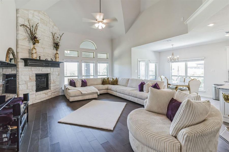 Living room featuring dark hardwood / wood-style floors, a stone fireplace, a towering ceiling, and ceiling fan with notable chandelier