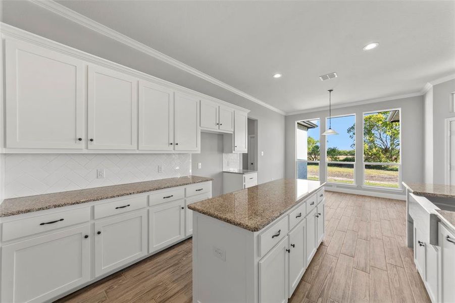 Kitchen featuring light stone countertops, a kitchen island, backsplash, white cabinets, and light hardwood / wood-style flooring