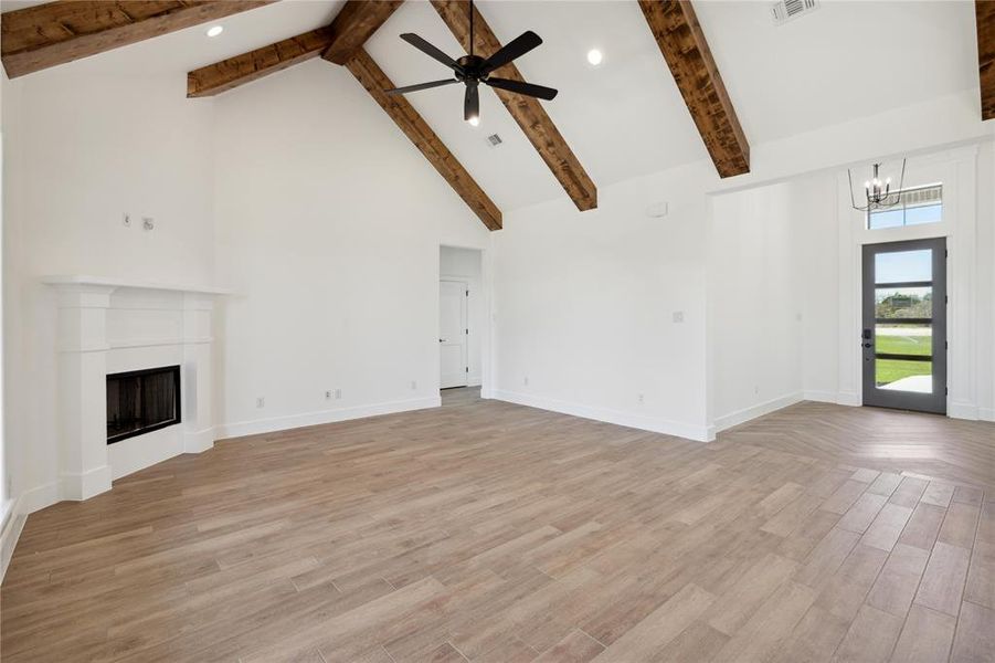 Unfurnished living room with ceiling fan with notable chandelier, beamed ceiling, light hardwood / wood-style flooring, and high vaulted ceiling