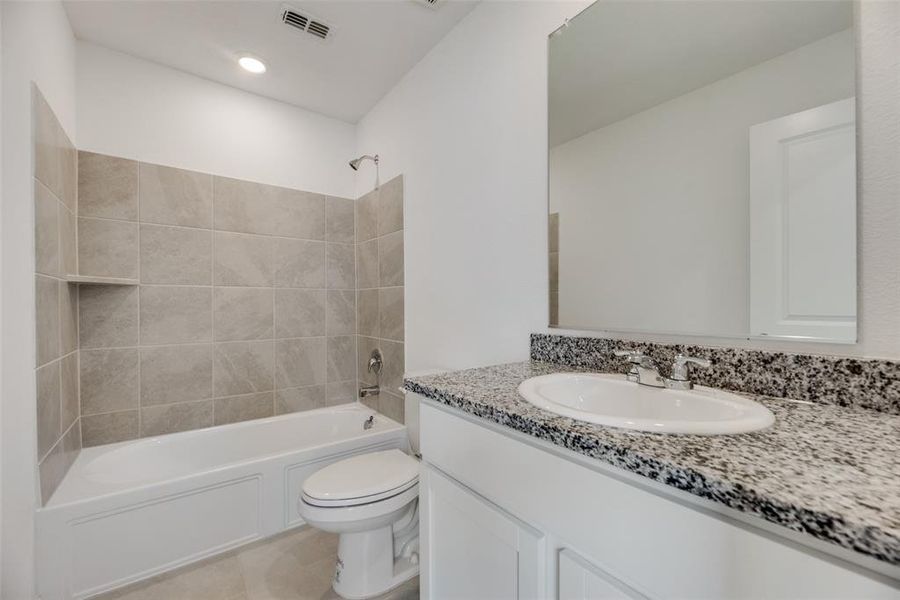 Full bathroom featuring tile patterned flooring, toilet, vanity, and tiled shower / bath