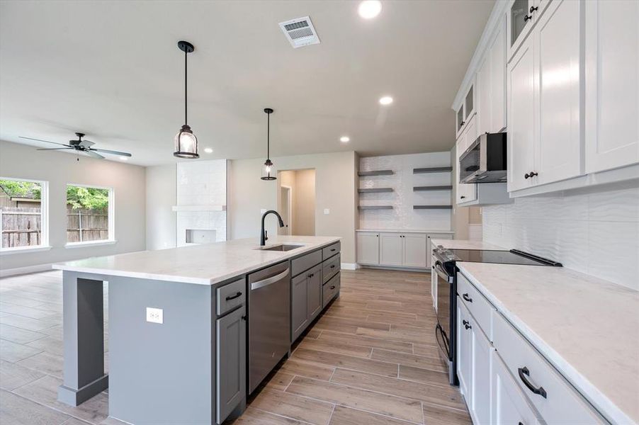 Kitchen with white cabinets, an island with sink, hanging light fixtures, appliances with stainless steel finishes, and decorative backsplash