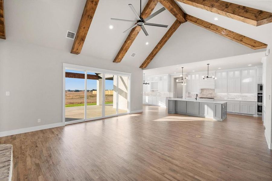 Unfurnished living room featuring sink, light wood-type flooring, ceiling fan with notable chandelier, beamed ceiling, and high vaulted ceiling