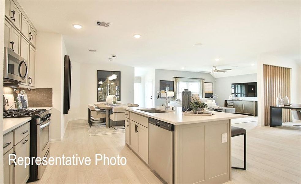 Kitchen with light wood-type flooring, stainless steel appliances, sink, ceiling fan, and a center island with sink