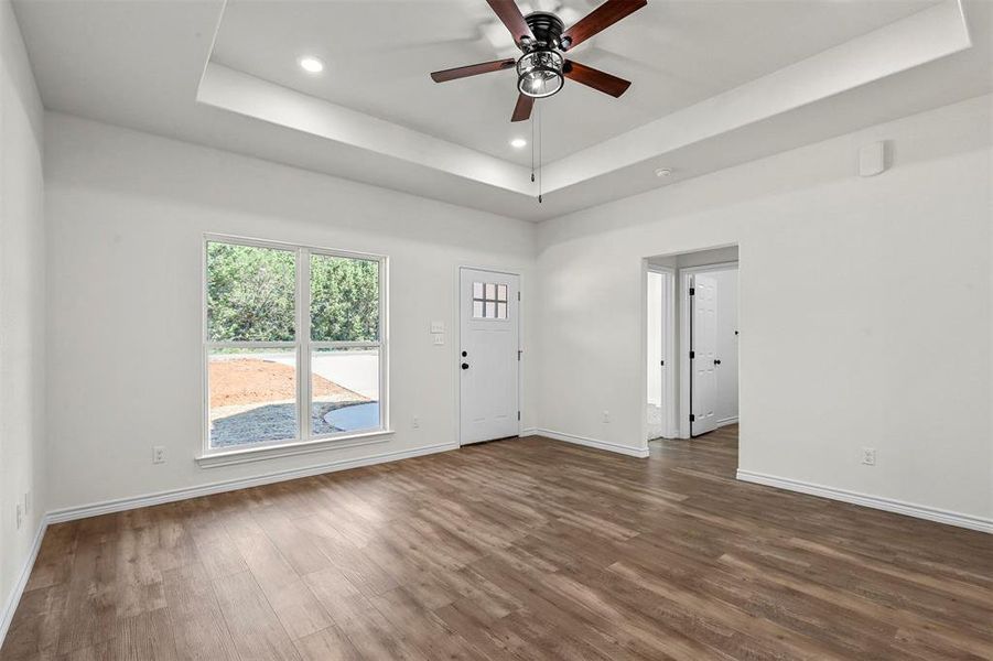 Unfurnished room with a tray ceiling, dark wood-type flooring, and ceiling fan
