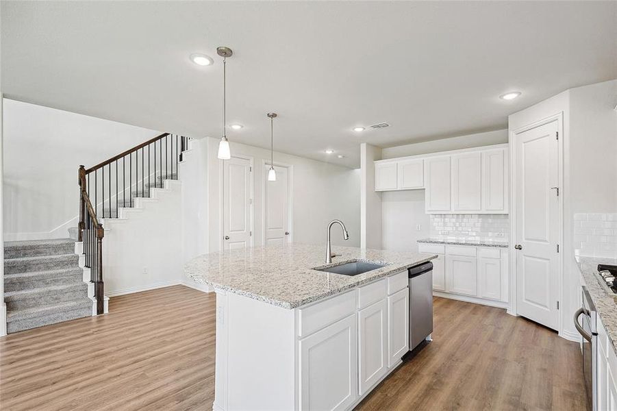 Kitchen with white cabinetry, an island with sink, light stone countertops, light wood-type flooring, and sink