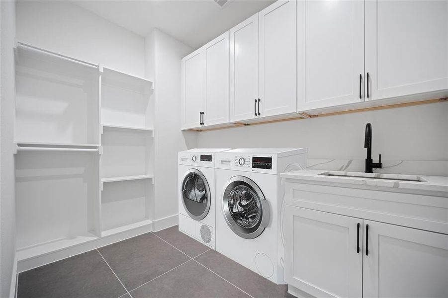Laundry room featuring sink, cabinets, dark tile patterned flooring, and separate washer and dryer