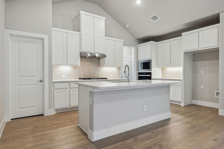 Kitchen with stainless steel appliances, backsplash, sink, white cabinets, and hardwood / wood-style flooring