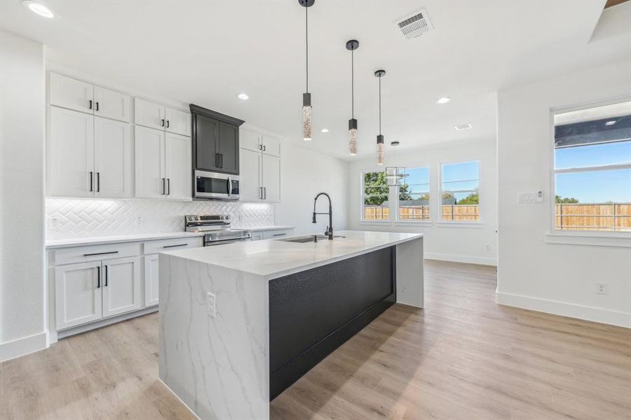 Kitchen with pendant lighting, a center island with sink, sink, light wood-type flooring, and appliances with stainless steel finishes