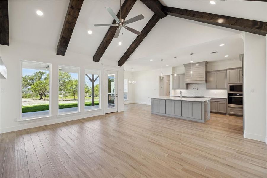 Unfurnished living room with ceiling fan with notable chandelier, light hardwood / wood-style floors, sink, high vaulted ceiling, and beam ceiling