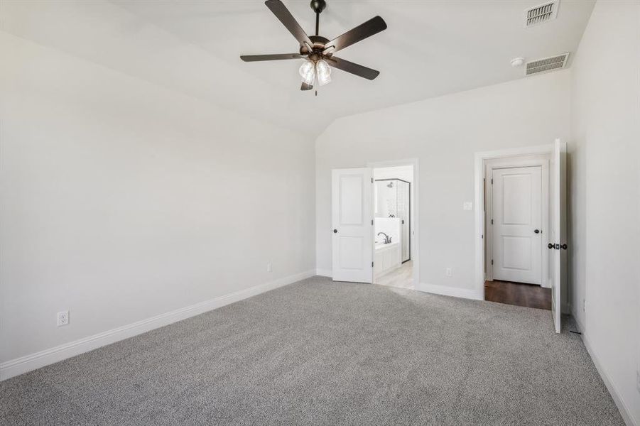Unfurnished bedroom featuring lofted ceiling, light colored carpet, ensuite bath, and ceiling fan