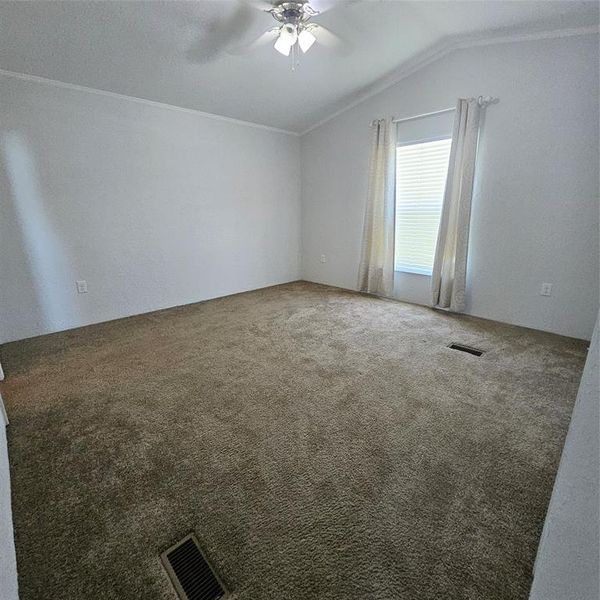 Carpeted empty room featuring crown molding, ceiling fan, and vaulted ceiling