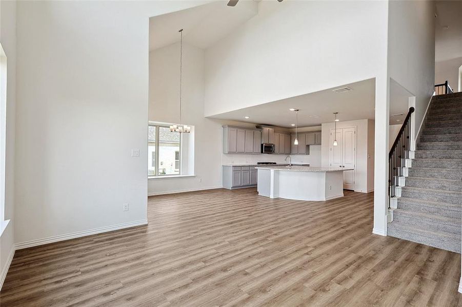 Unfurnished living room featuring light hardwood / wood-style flooring, high vaulted ceiling, sink, and ceiling fan with notable chandelier