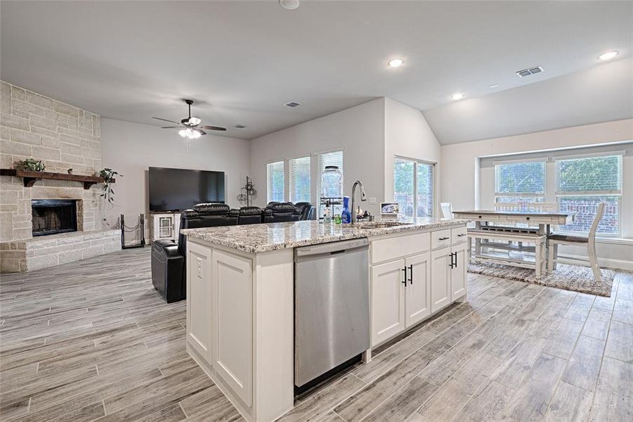 Kitchen featuring a kitchen island with sink, sink, light wood-type flooring, stainless steel dishwasher, and white cabinetry