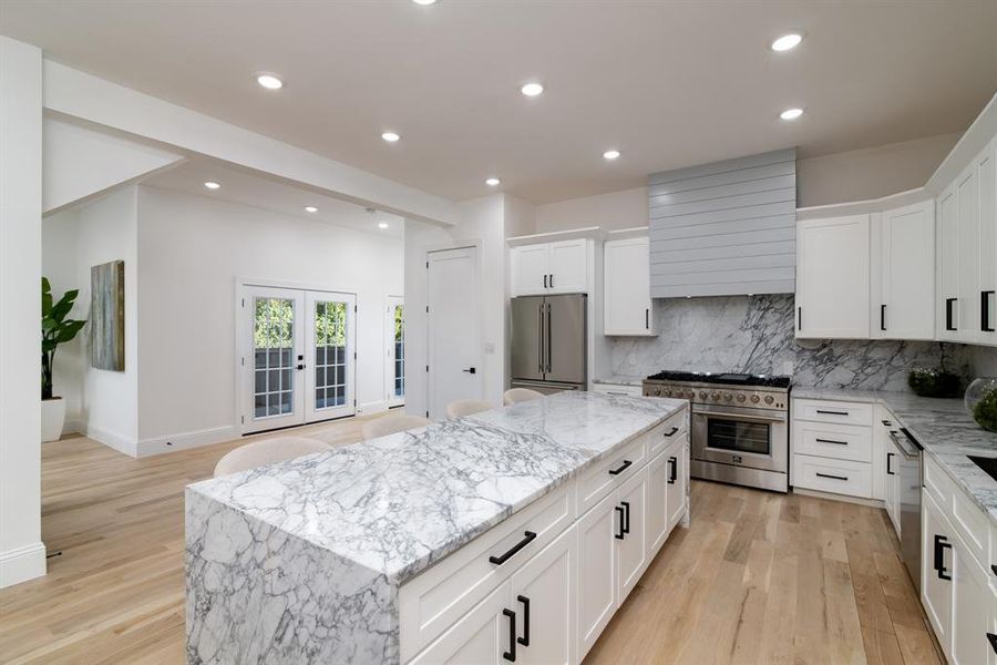 Kitchen featuring high end appliances, light hardwood / wood-style flooring, white cabinetry, and a kitchen island