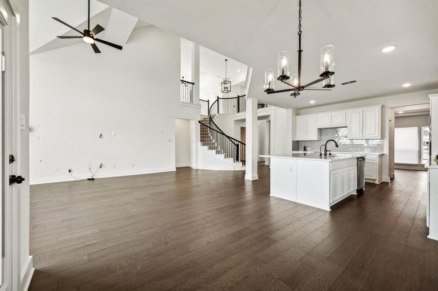 Kitchen featuring white cabinets, ceiling fan with notable chandelier, dark wood-type flooring, pendant lighting, and a center island with sink