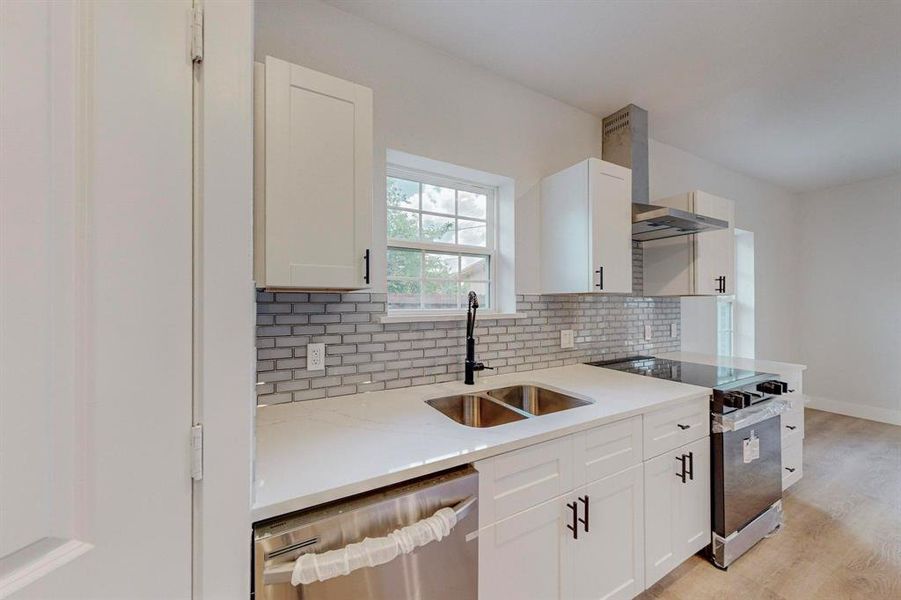 Kitchen featuring light hardwood / wood-style flooring, backsplash, wall chimney exhaust hood, sink, and appliances with stainless steel finishes