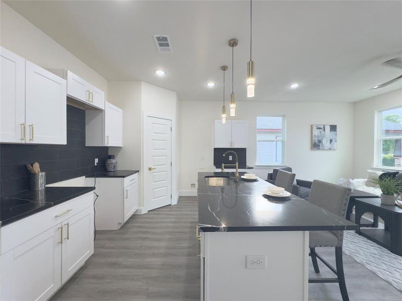 Kitchen with pendant lighting, an island with sink, dark wood-type flooring, a kitchen bar, and sink