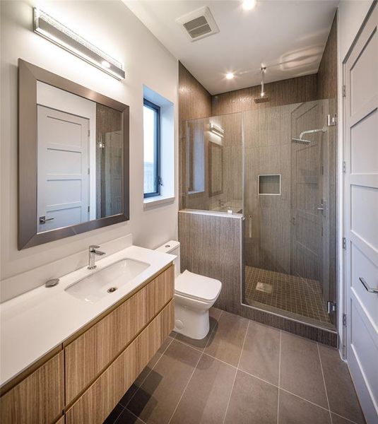 En-suite secondary bathroom with custom built vanity, framed mirror, wall sconce and enclosed walk-in shower with porcelain tile walls