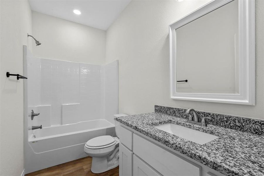 Full bathroom with vanity with extensive cabinet space, washtub / shower combination, toilet, and wood-type flooring