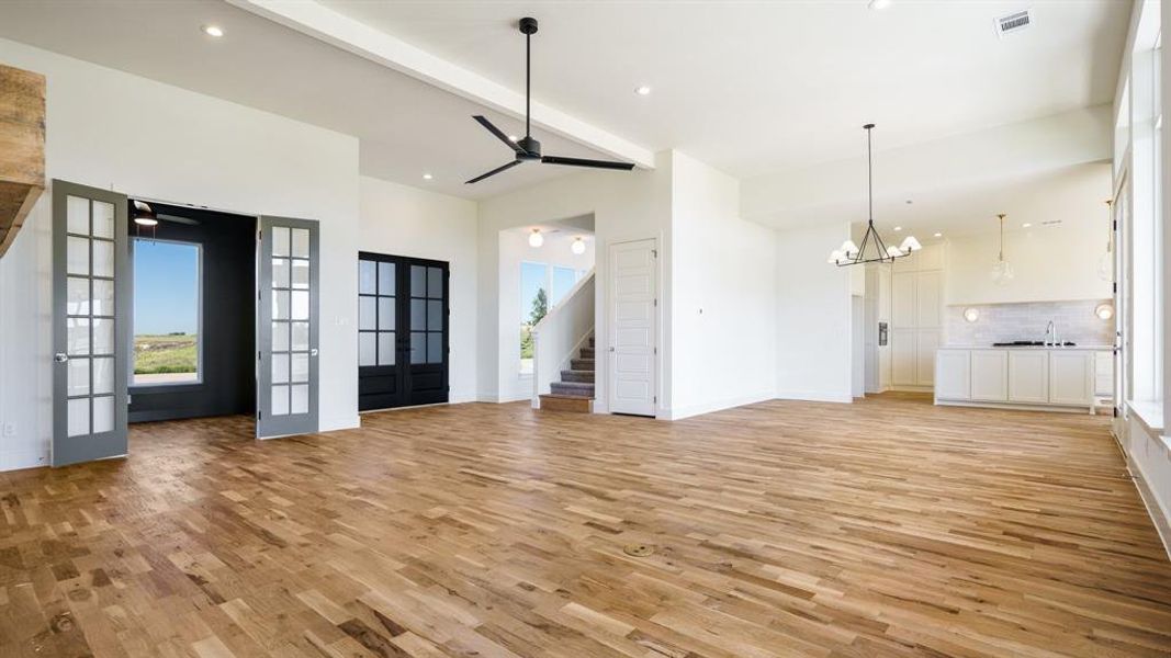 Unfurnished living room featuring sink, light wood-type flooring, ceiling fan with notable chandelier, french doors, and beamed ceiling