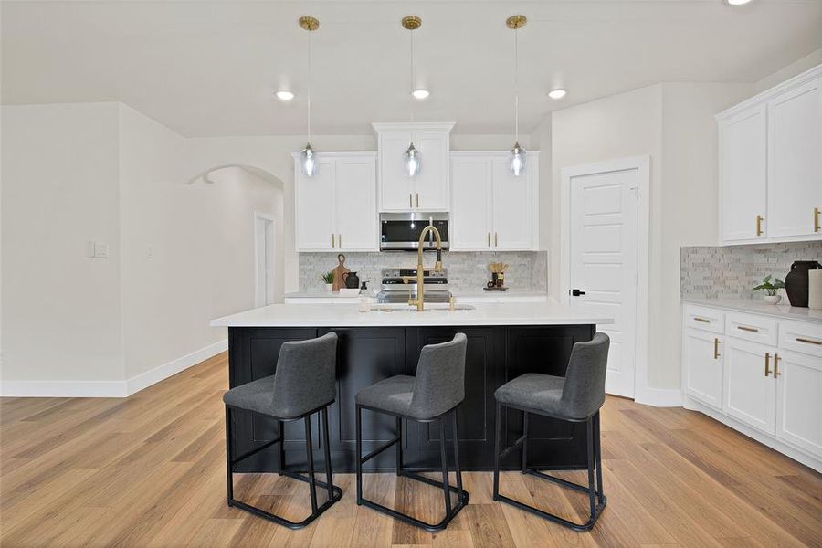 Kitchen with light hardwood / wood-style flooring, backsplash, a kitchen island with sink, stainless steel appliances, and white cabinetry