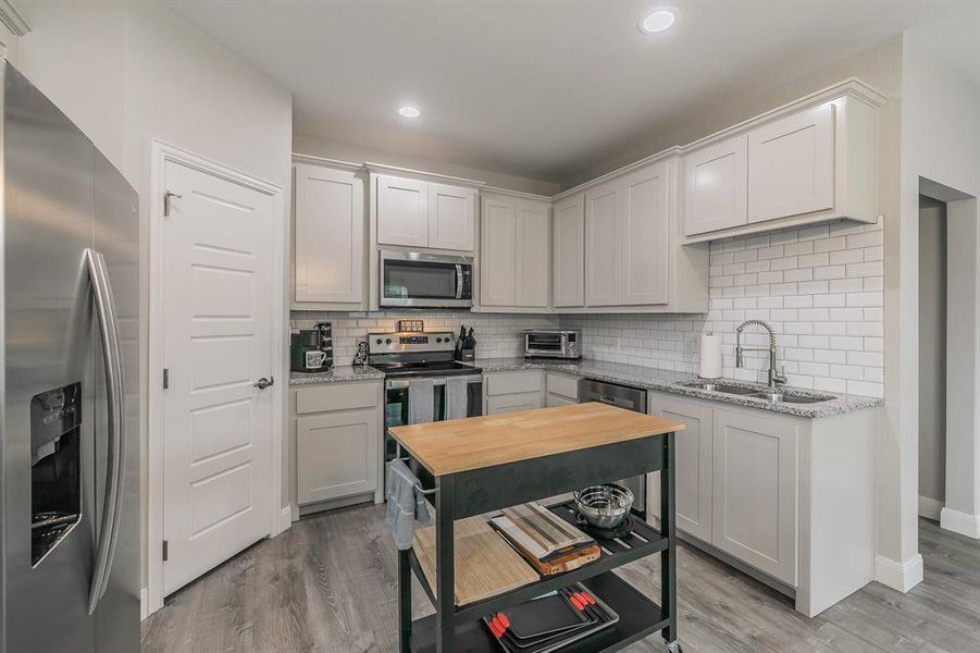 Kitchen featuring stainless steel appliances, sink, light hardwood / wood-style flooring, and backsplash