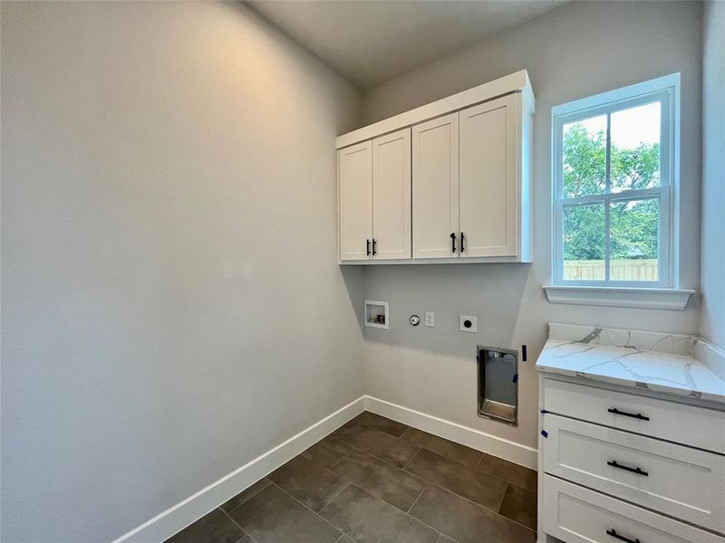 Clothes washing area featuring dark tile patterned floors, hookup for a gas dryer, electric dryer hookup, washer hookup, and cabinets