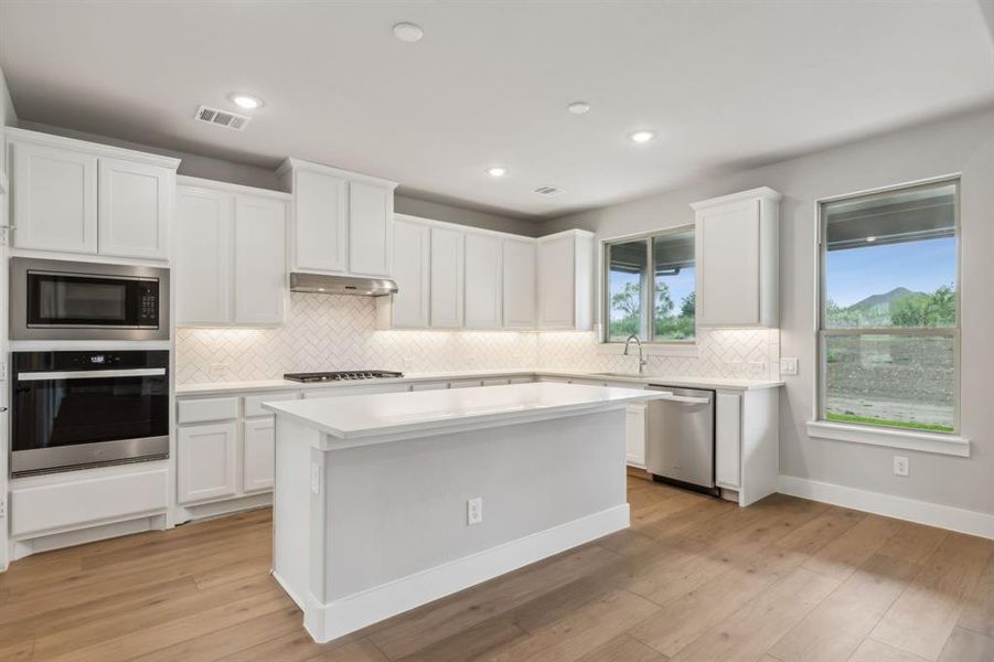 Kitchen with stainless steel appliances, light wood-type flooring, and white cabinetry