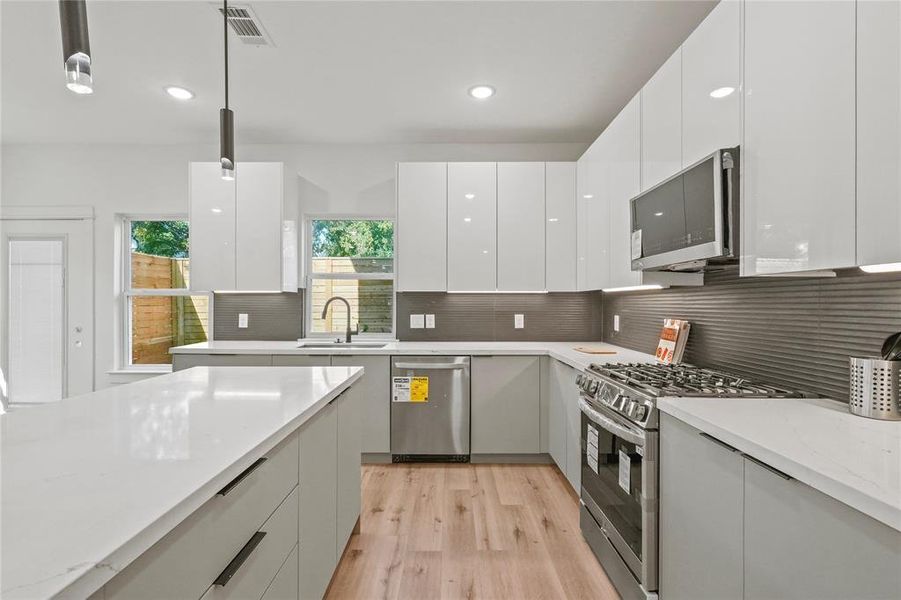 Kitchen featuring appliances with stainless steel finishes, sink, decorative light fixtures, and white cabinetry