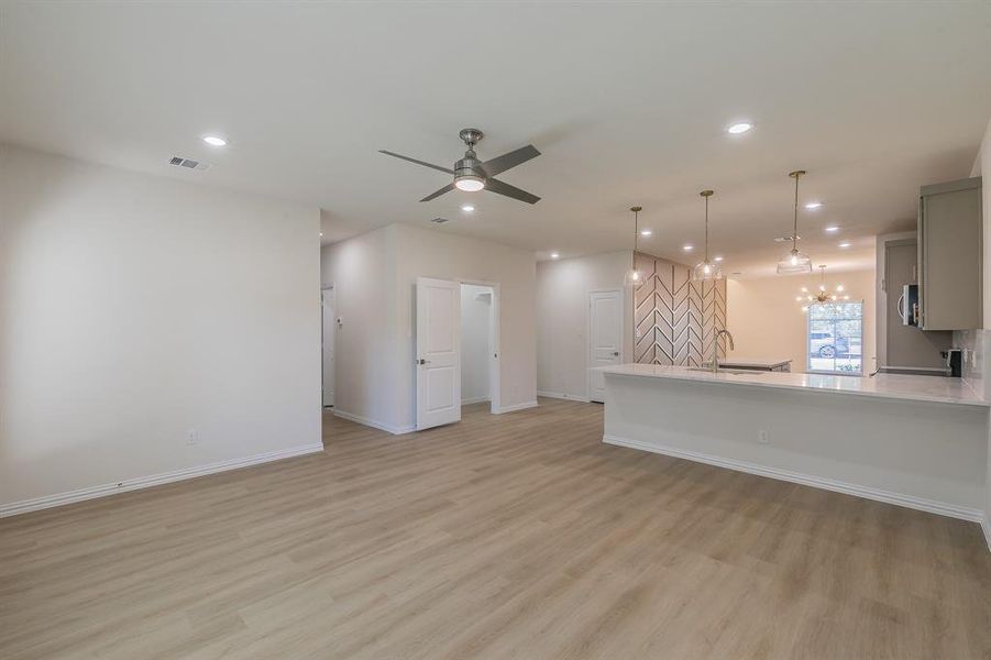 Unfurnished living room featuring ceiling fan with notable chandelier and light hardwood / wood-style flooring