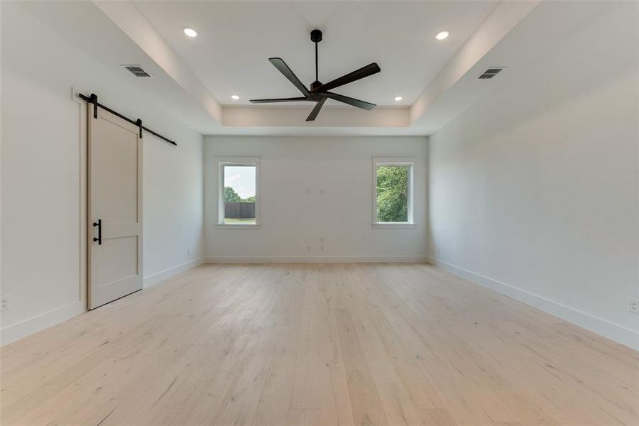 Spare room with light wood-type flooring, ceiling fan, a raised ceiling, and a barn door