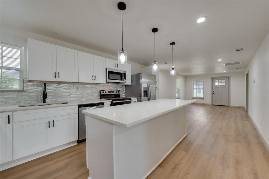 Kitchen with a kitchen island, light wood-type flooring, white cabinets, sink, and appliances with stainless steel finishes