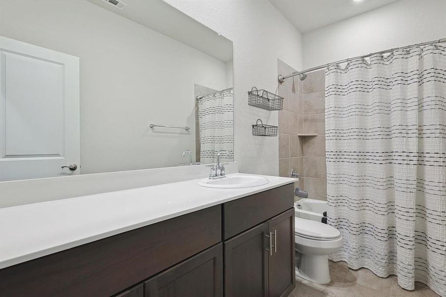 Full bathroom featuring shower / bathtub combination with curtain, vanity, toilet, and tile floors