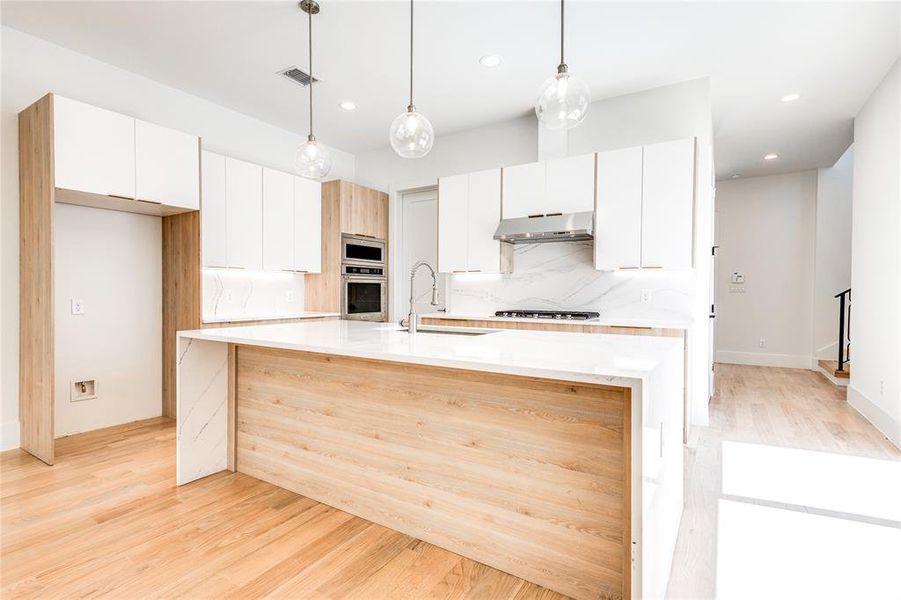 Kitchen with stainless steel appliances, light hardwood / wood-style floors, tasteful backsplash, and wall chimney range hood