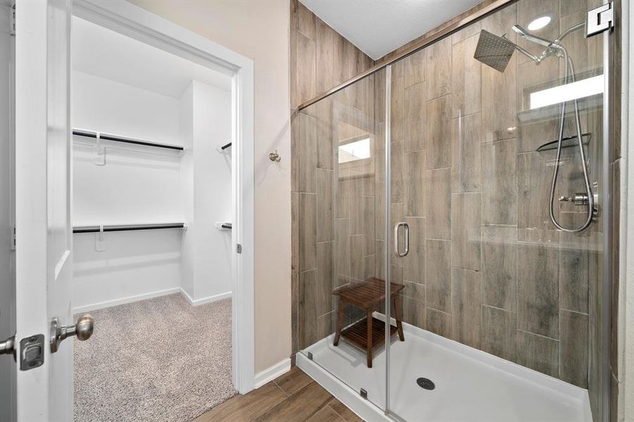 This additional view of the primary bath showcases a walk-in shower with tile surround and the spacious walk-in closet with shelving.