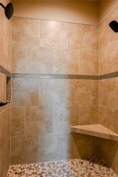 Primary shower has custom tile accents, shampoo shelf and dual shower heads.