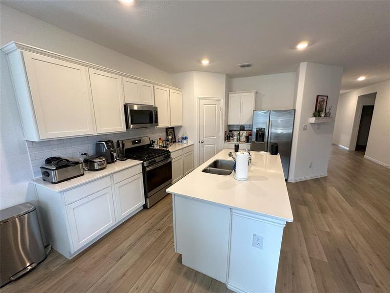 Kitchen featuring white cabinets, appliances with stainless steel finishes, a center island with sink, and light hardwood / wood-style floors