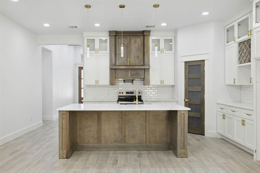 Kitchen featuring an island with sink, stainless steel range oven, pendant lighting, and light wood-type flooring