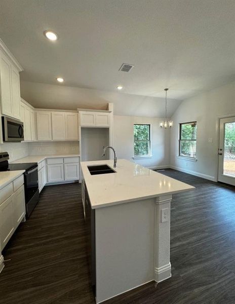 Kitchen with an island with sink, sink, decorative light fixtures, white cabinetry, and black / electric stove