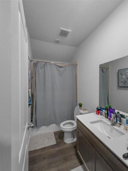 Full bathroom with vanity, lofted ceiling, wood-type flooring, toilet, and shower / tub combo with curtain