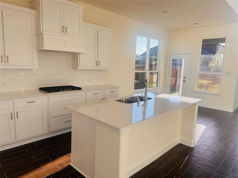 Kitchen featuring dark hardwood / wood-style floors, sink, white cabinets, a center island with sink, and gas stovetop