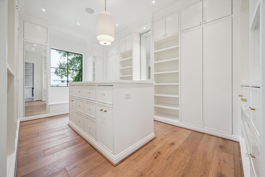 This expansive primary closet is designed for ultimate organization, featuring multiple hanging rods, a convenient packing station, and open shelving for easy access to your wardrobe. As the larger of two closets, it offers ample space to keep everything beautifully arranged and within reach.