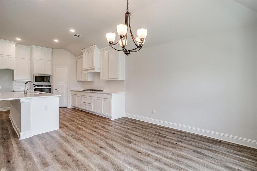 Kitchen with hanging light fixtures, light wood-type flooring, tasteful backsplash, and stainless steel appliances