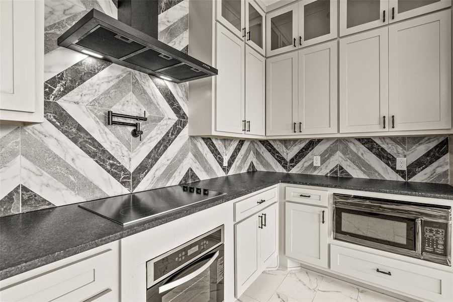 Kitchen with black appliances, white cabinets, wall chimney exhaust hood, tasteful backsplash, and light tile floors