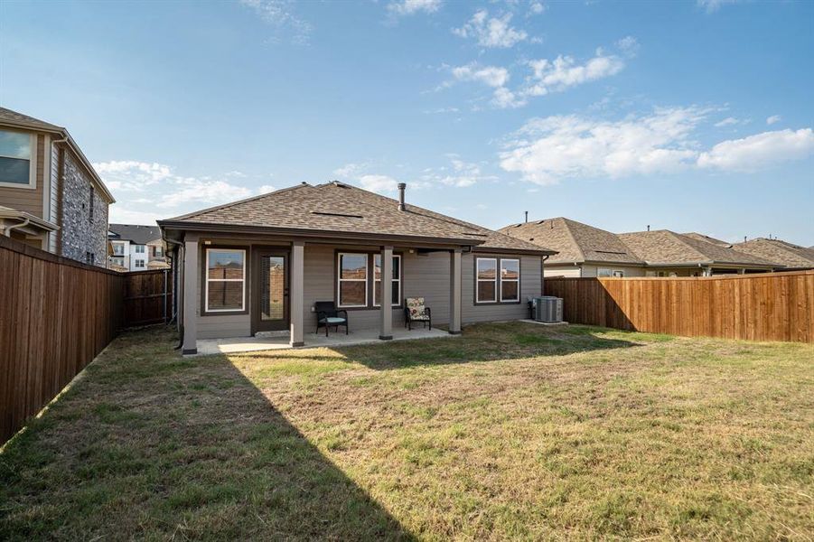 Rear view of property featuring a yard, central AC unit, and a patio area