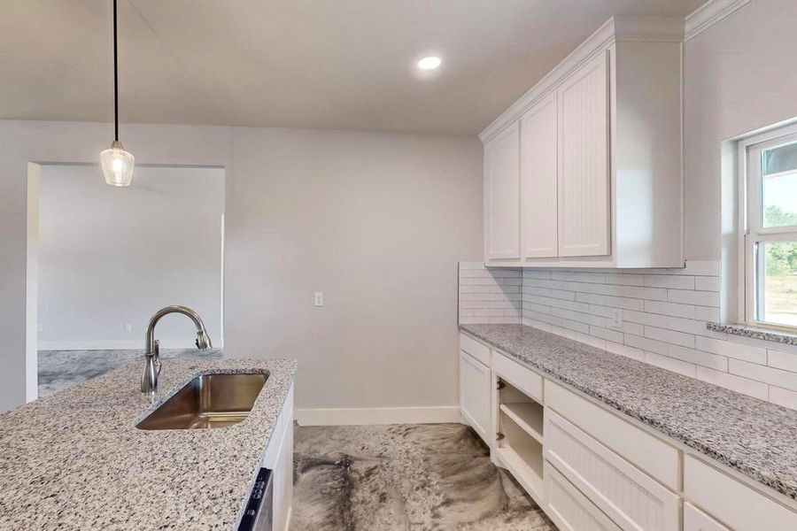 Kitchen featuring tasteful backsplash, white cabinets, light stone counters, pendant lighting, and sink