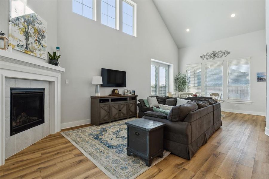 Living room featuring high vaulted ceiling with high windows, a tile fireplace and wood look luxury pland vinyl flooring