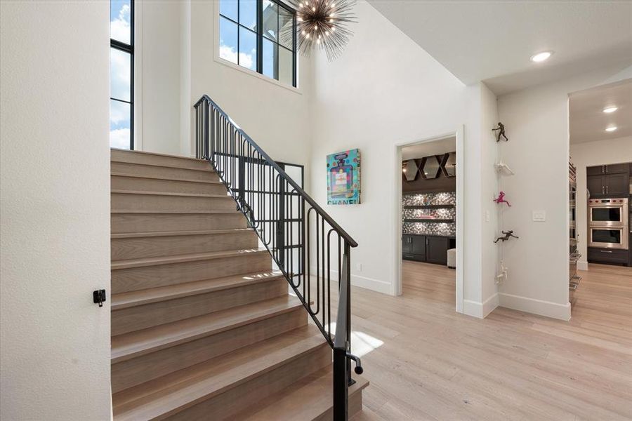 Staircase with a towering ceiling, hardwood / wood-style floors, and a notable chandelier